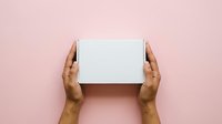 Hands holding white box on pink background for product packaging, unboxing, delivery, and retail presentation concepts.