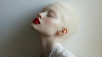 Young woman with platinum blonde hair and red lips in profile pose against neutral background for beauty and fashion concepts.