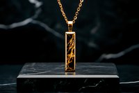 Elegant gold pendant necklace with delicate organic pattern encased in rectangular frame, displayed on dark marble surface against black background.