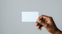 Hand holding blank white business card against neutral gray background for branding and corporate identity mockup purposes.
