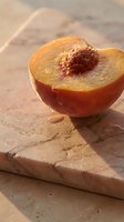 Fresh peach half with pit exposed on neutral stone surface, showcasing juicy flesh and natural texture for food styling and culinary projects.
