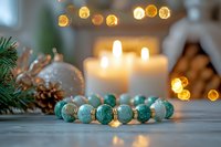 Turquoise gemstone bracelet with burning candles and Christmas decorations on wooden table, soft bokeh lights creating cozy festive atmosphere.