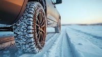 Off-road tire with aggressive tread pattern on snowy winter road, close-up view showing detailed tire tracks in fresh snow during cold weather conditions.