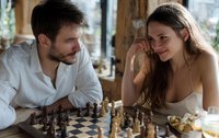 Young couple playing chess in cozy cafe, sharing intimate moment over strategic game with natural light streaming through windows.