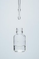 Clear water drops falling into glass bottle filled with transparent liquid against white background, minimalist composition capturing motion and purity.