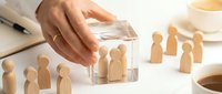Business protection concept with hand covering wooden figures under glass shield representing employee safety and corporate security measures.