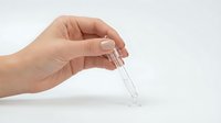 Hand holding glass test tube with clear liquid for laboratory research and scientific experiments on white background.