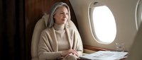 Confident mature Caucasian businesswoman in beige sweater working on documents during luxury private jet flight for corporate travel and executive lifestyle.