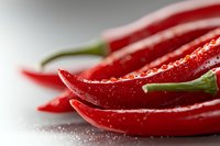 Fresh red chili peppers with water drops and salt crystals on white surface, extreme close up macro photography showing vibrant color and texture.