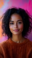 Young mixed race woman with curly black hair and natural makeup smiling confidently against vibrant pink and purple background wearing orange knit sweater.