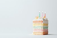 Slice of pastel rainbow layered birthday cake with white frosting and lit candles on light background. Minimal celebration dessert composition.