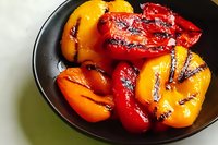 Grilled red and yellow bell peppers with charred marks served on black plate, close up view showing vibrant colors and roasted texture for food photography.