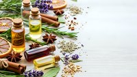 Natural essential oils in glass bottles with aromatic herbs and spices on white wooden background for aromatherapy wellness and spa treatments.