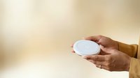 Hands holding empty white plate against blurred beige background, suitable for food service, restaurant marketing, and culinary content.