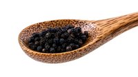 Whole black peppercorns in wooden spoon isolated on white background, macro shot of aromatic spice ingredient for cooking and seasoning food.