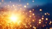 Magical glowing golden bokeh lights and sparkles on dark blue background with bright sunburst effect, creating festive atmosphere for holiday designs.