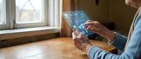 Senior man using transparent futuristic tablet device with holographic interface display in modern home interior for digital technology innovation.