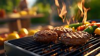 Juicy beef burgers grilling on barbecue grill with flames and vegetables in blurred background during outdoor summer cooking session.