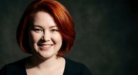 Professional portrait of confident middle-aged Caucasian businesswoman with red bob haircut smiling warmly against dark background for corporate use.