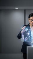 Professional Asian businesswoman in suit interacting with futuristic holographic interface displaying data analytics and digital charts in modern office.