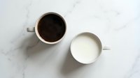 Black coffee in white ceramic mug and milk in matching cup on marble surface, overhead view for beverage, breakfast, and cafe concepts.
