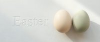 Two pastel Easter eggs in cream and sage green rest on a white surface with embossed Easter text, casting soft shadows for a minimal spring holiday design.