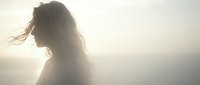 Young woman with flowing hair in dreamy backlit atmosphere creating ethereal silhouette against soft golden light for wellness and beauty concepts.