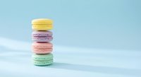 Colorful French macarons stacked on pastel blue background. Sweet dessert tower with yellow, purple, pink and mint green cookies for bakery menu.