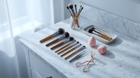 Professional makeup brushes and beauty tools arranged on white marble vanity counter for cosmetic application and skincare routine.