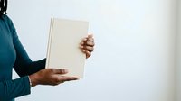 Person with medium skin tone wearing teal long-sleeve shirt holding open blank book or journal against white background, suitable for education, publishing, and learning concepts.