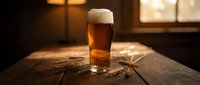 Fresh golden beer with white foam head in glass on rustic wooden table with wheat stalks in warm ambient lighting for brewery and pub concepts.