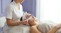 Professional cosmetologist applying facial treatment to relaxed client in modern spa salon with natural lighting for skincare and wellness services.