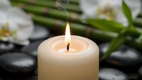 Burning candle with white orchids and black stones creating peaceful spa atmosphere for relaxation and wellness treatments.