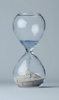 Glass hourglass with green plant sprout growing from cracked dry earth, symbolizing time, growth, and environmental renewal on neutral background.