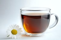 Glass cup of black tea with fresh chamomile flower on white background, close up view. Herbal drink concept for relaxation and wellness.