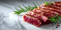 Juicy grilled beef steak sliced on marble board with fresh rosemary sprigs and peppercorns, showcasing medium-rare doneness for gourmet food photography.