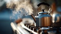 Shiny metal kettle with steam rising on gas stove, creating cozy atmosphere in kitchen during tea preparation.
