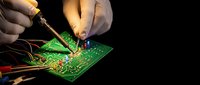 Electronics technician soldering components on green circuit board with precision tools for repair and assembly work in professional workshop environment.