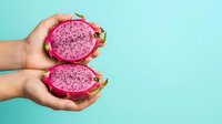Hands holding halved pink dragon fruit with vibrant magenta flesh against turquoise background, suitable for food, nutrition, and wellness marketing materials.