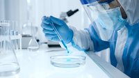 Scientist in protective equipment conducting laboratory research with pipette and petri dish in modern medical facility for pharmaceutical development.