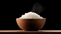Steaming white jasmine rice served in traditional clay bowl on wooden surface against dark background. Steam rises creating atmospheric food scene.