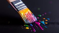 Vibrant paint brush with colorful drips and splatters against dark background, capturing creative artistic expression in macro photography. Dramatic lighting highlights rainbow hues.