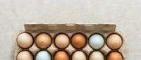 Farm fresh organic eggs in cardboard carton showing variety of natural brown and white shell colors from free range chickens on rustic linen background.