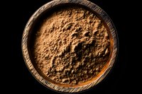 Ground cinnamon powder in rustic wooden bowl on black background, dramatic side lighting creates texture and shadows, macro food photography.