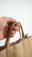 Hand holding natural jute shopping bag handle on white background, eco-friendly reusable carrier for sustainable lifestyle and zero waste shopping.