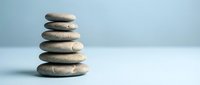 Balanced stack of smooth river stones creating zen meditation tower on clean white surface against soft blue background for wellness and mindfulness concepts.