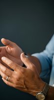Two men shaking hands in business agreement, closeup of diverse male hands with wedding ring and watch against dark background for corporate partnership concepts.