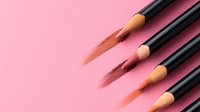 Wooden black pencils with brown color strokes on pink background, diagonal composition with copy space. Minimalist makeup and cosmetics concept.