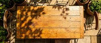 Wooden table with dappled sunlight and shadow patterns, surrounded by potted plants and vintage chairs, overhead view for interior design and home decor projects.