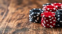 Stacked red and black poker chips on rustic wooden table with dramatic lighting and shallow depth of field, creating atmospheric casino gaming ambiance.